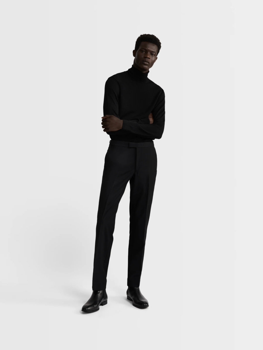 A man modeling the black T.M.Lewin Lancewood Trousers paired with a black T.M.Lewin merino roll neck and black Chelsea Boots