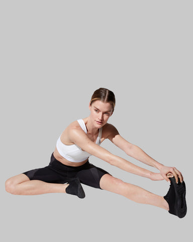 woman stretching after workout wearing CW-X compression pant and sports bra