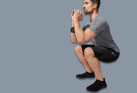 male athlete squatting holding dumbbell wearing stabilyx ventilator shorts in black and a grey t-shirt
