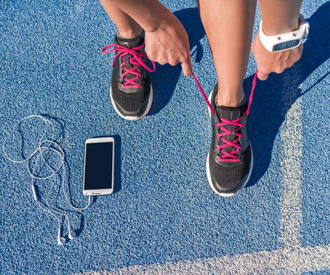 runner tying her shoes with phone and earphones laying next to her