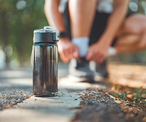 runner training tying his shoe taking a break to hydrate with his water bottle