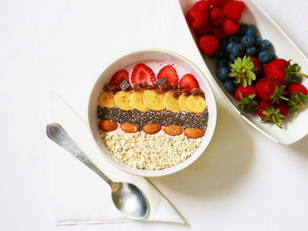 yogurt bowl with oats, nuts, seeds, bananas, strawberries with a side bowl of raspberries, blueberries, strawberries