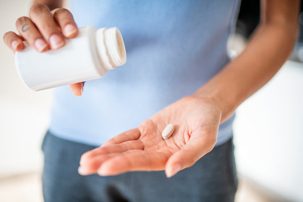 a woman pouring a magnesium supplement into his other hand from the white bottle