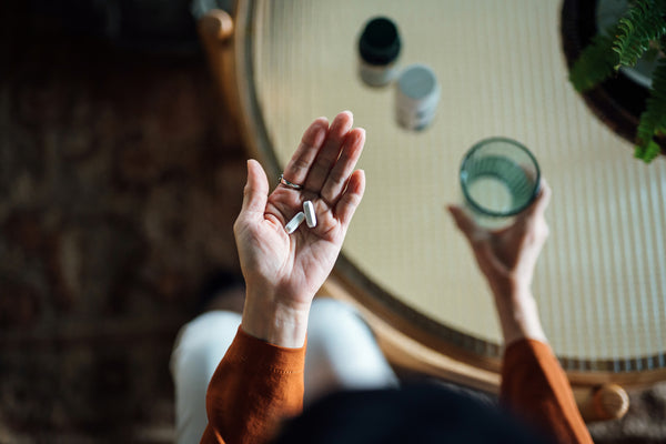 Overhead view of senior Asian woman feeling sick, taking medicines in hand with a glass of water at home