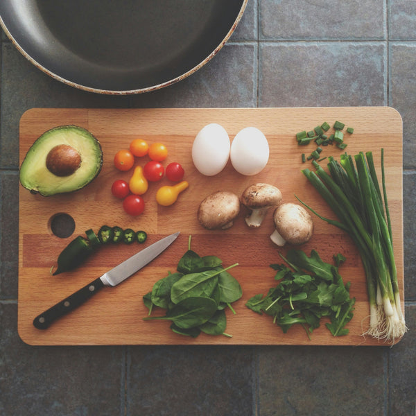 healthy, anti-inflammatory foods on a cutting board such as avocado, tomatoes, dark leafy greens, eggs, mushrooms