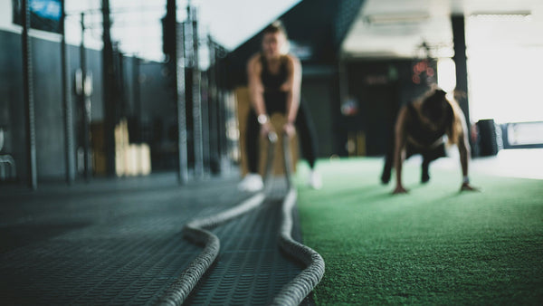 a woman using battle ropes at the gym with another woman by her side doing push ups