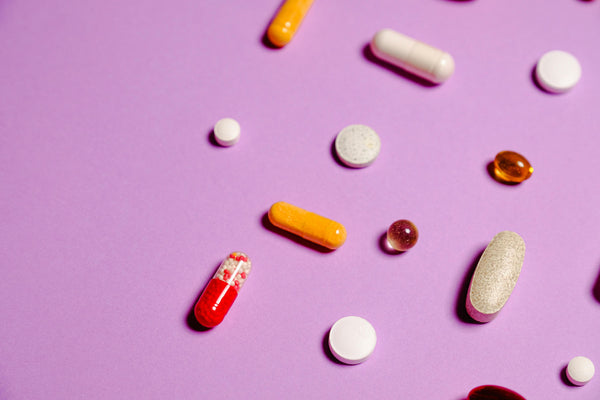 variety of supplement pills, tablets, and capsules on a purple background