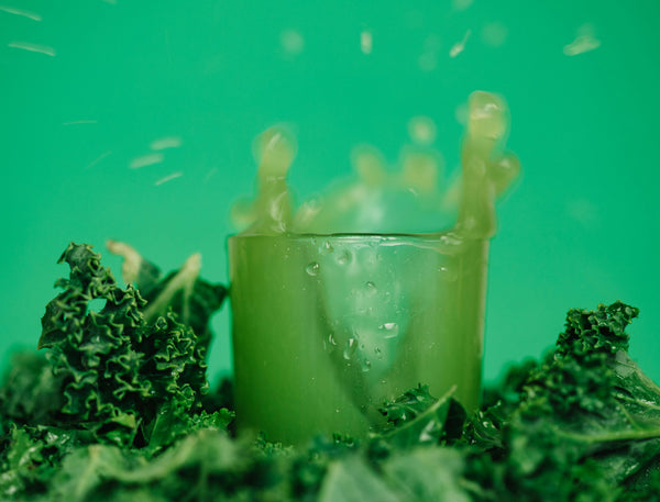 green juice in a glass with leafy greens around it and a green background