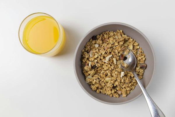 a bowl of granola with oats and fried fruit and a glass of orange juice