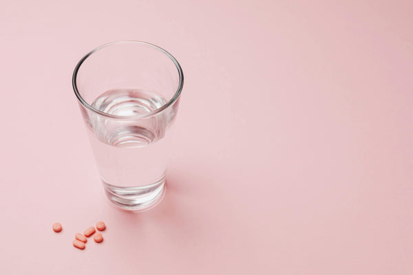 supplements and a glass of water on a light pink background