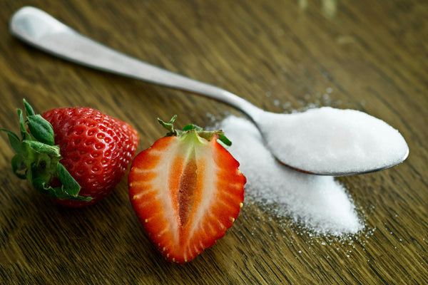 sugar on a spoon next to a sliced strawberry, sitting on a wood table top