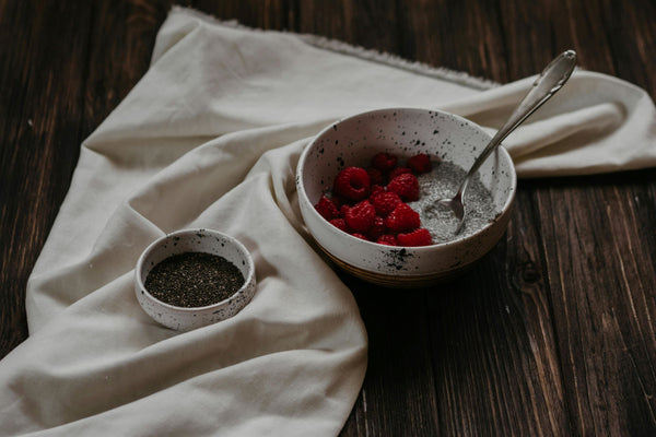 bowl of chia seed pudding with raspberries and bowl of chia seeds