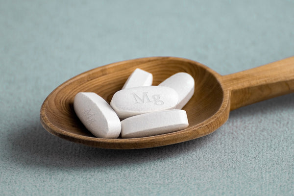 Tablets, vitamins with the abbreviation Mg (magnesia, the macronutrient magnesium) lying in a wooden spoon on a light background.