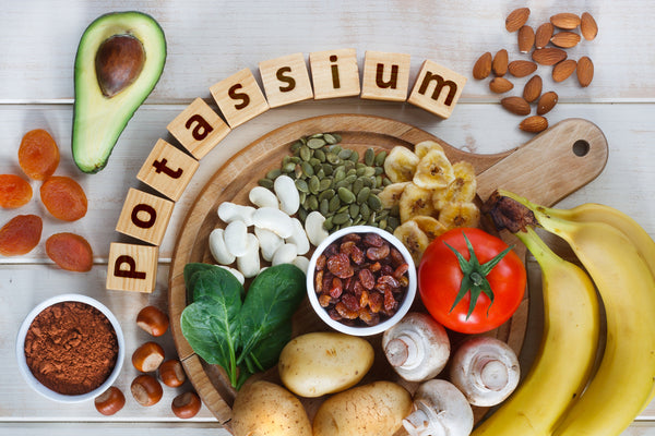 Potassium spelled out in wooden blocks with potassium rich foods around it including bananas, avocados, nuts, potatoes and others