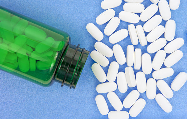 magnesium pills on a blue surface with a green magnesium supplement bottle beside them