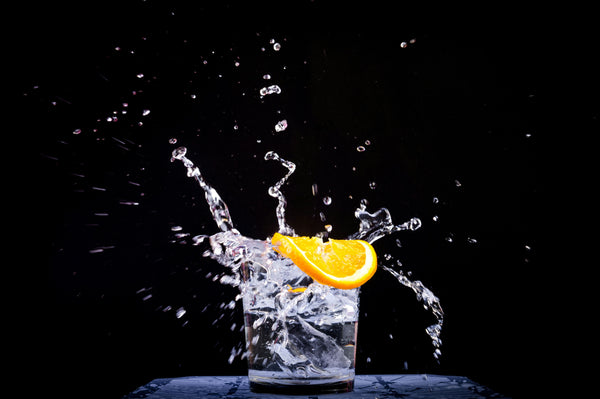 glass of water splashing with a slice of orange on the rim