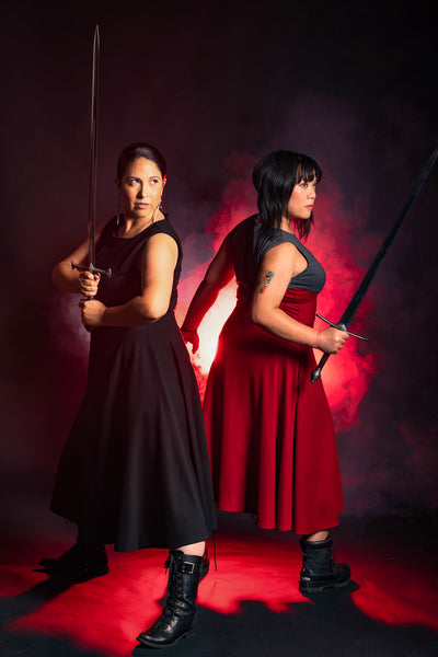 Natalie and Cheryll back to back wielding swords and wearing the Fighter Longsword Dress
