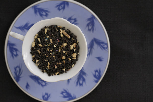 A top down view of a a tea cup and saucer. The tea cup is filled with Bard's Blend tea from Friday Afternoon Tea. The saucer under the cup is light blue with a dark blue feather motif.