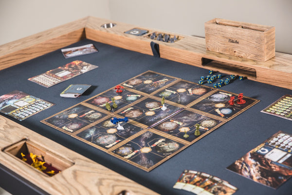 The Phalanx table with the top removed. A game is set up on a game mat that is inset into the table. Along the edges are cup holders, dice tower, and carved holders for game pieces. 