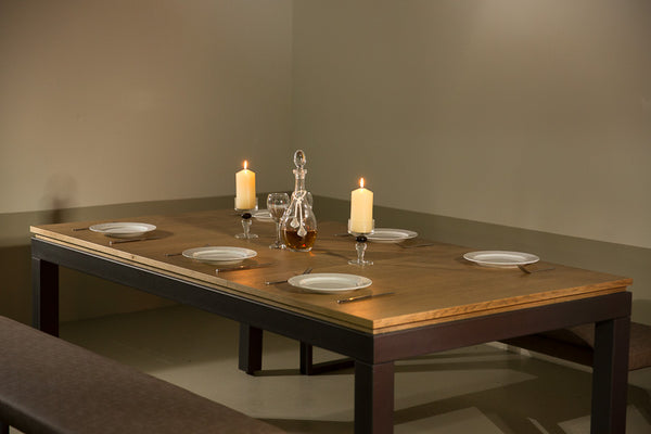 A metal and wood table from Rathskellers. The table is set for a meal with plates, utensils, and candles.