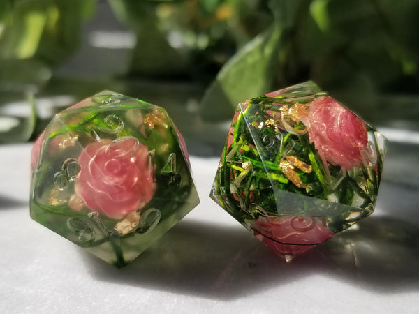 Two D20s with unpainted numbers. The D20s are made of clear resin with roses and vines on the inside.