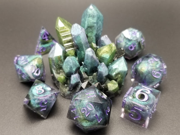 A set of purple, green, and teal dice surrounding a matching resin crystal.