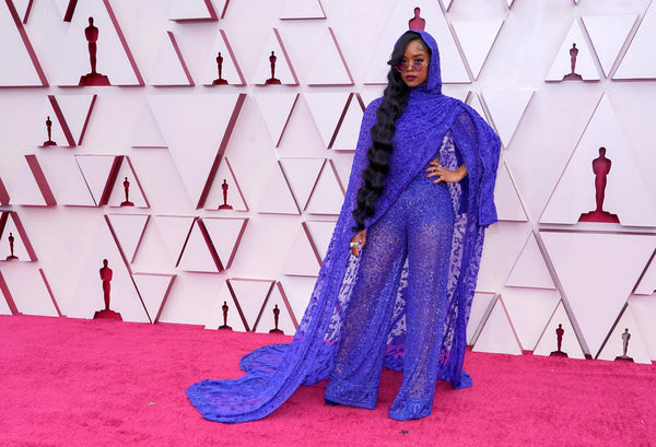 H.E.R. wearing a bright indigo ensemble by Dundas. The mesh body suit has a large hooded shawl draped across it.