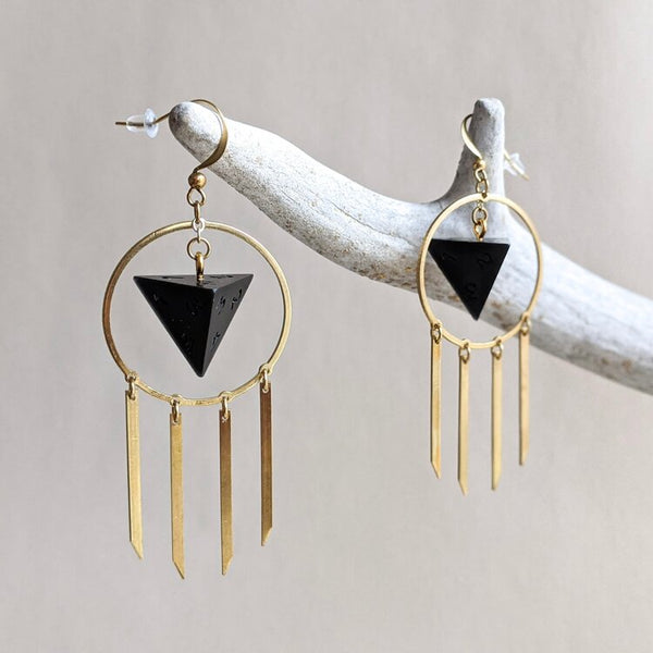 A set of earrings created with resin D4 dice. The dice are opaque black surrounded by a gold metal wire and gold metal bars. Created by Yaniir