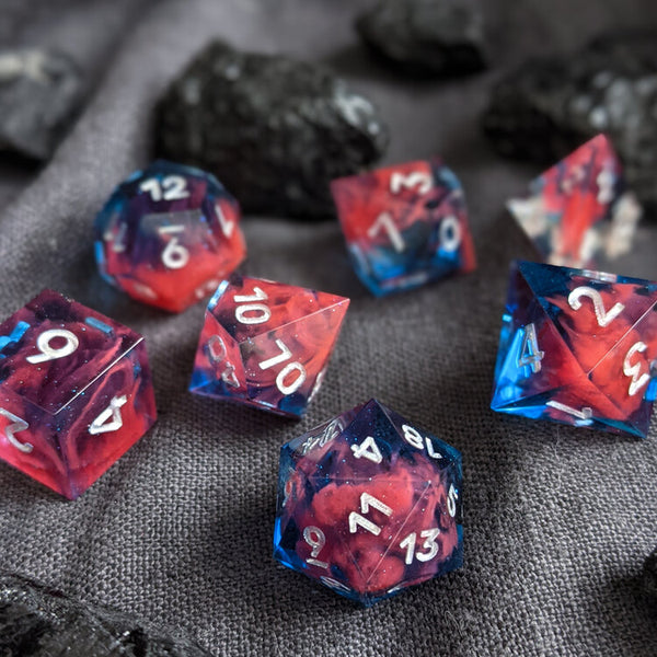 A set of handcrafted resin tabletop rpg dice ranging from D20 to a D4. The colors are blue and red with white painted numbers. Created by Yaniir