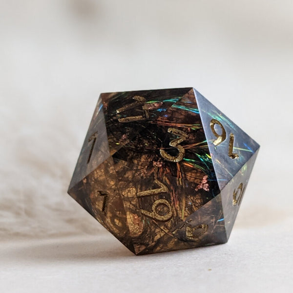 A handcrafted resin tabletop rpg D20 dice. The dice is translucent brown with holographic foil inside. Created by Yaniir