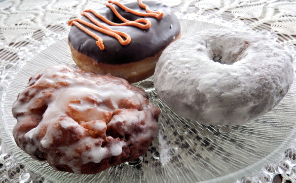 A plate of three donuts. One donut is powdered, another is glazed, and the third is chocolate frosted.