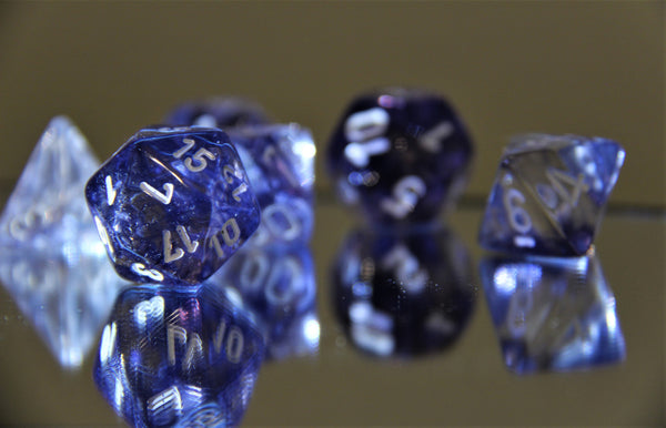 A photo of purple resin polyhedral dice. In the foreground you can see a D20 and the other dice are blurred out in the background.