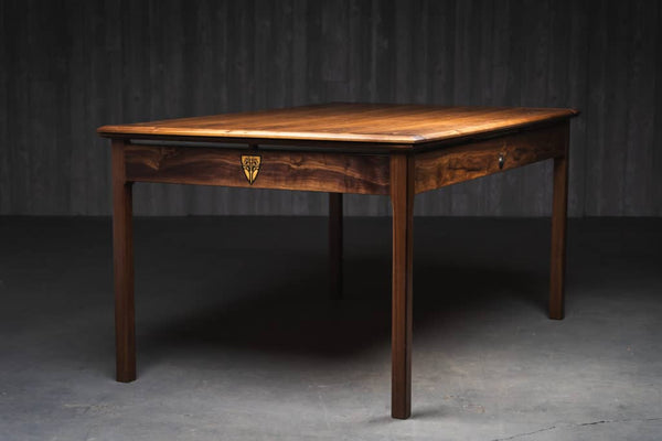 A photo of the Sojourn gaming table in a dark wood. You can see the logo for Wyrmwood an the shorter end of the table.