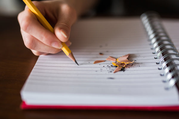An image of someone writing in a notebook with a pencil. There are pencil shavings on the paper.