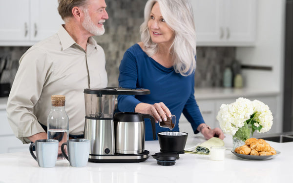 Woman is pouring coffee grinds into brewer filter.