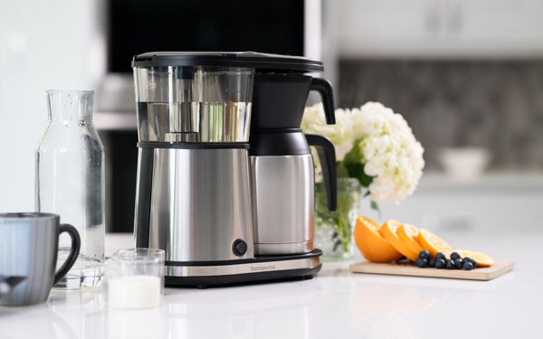 8-cup coffee brewer sitting on a kitchen counter top next to fruitboard.