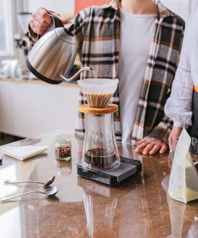A man in a plaid shirt is pouring water from a kettle to make pour over coffee.