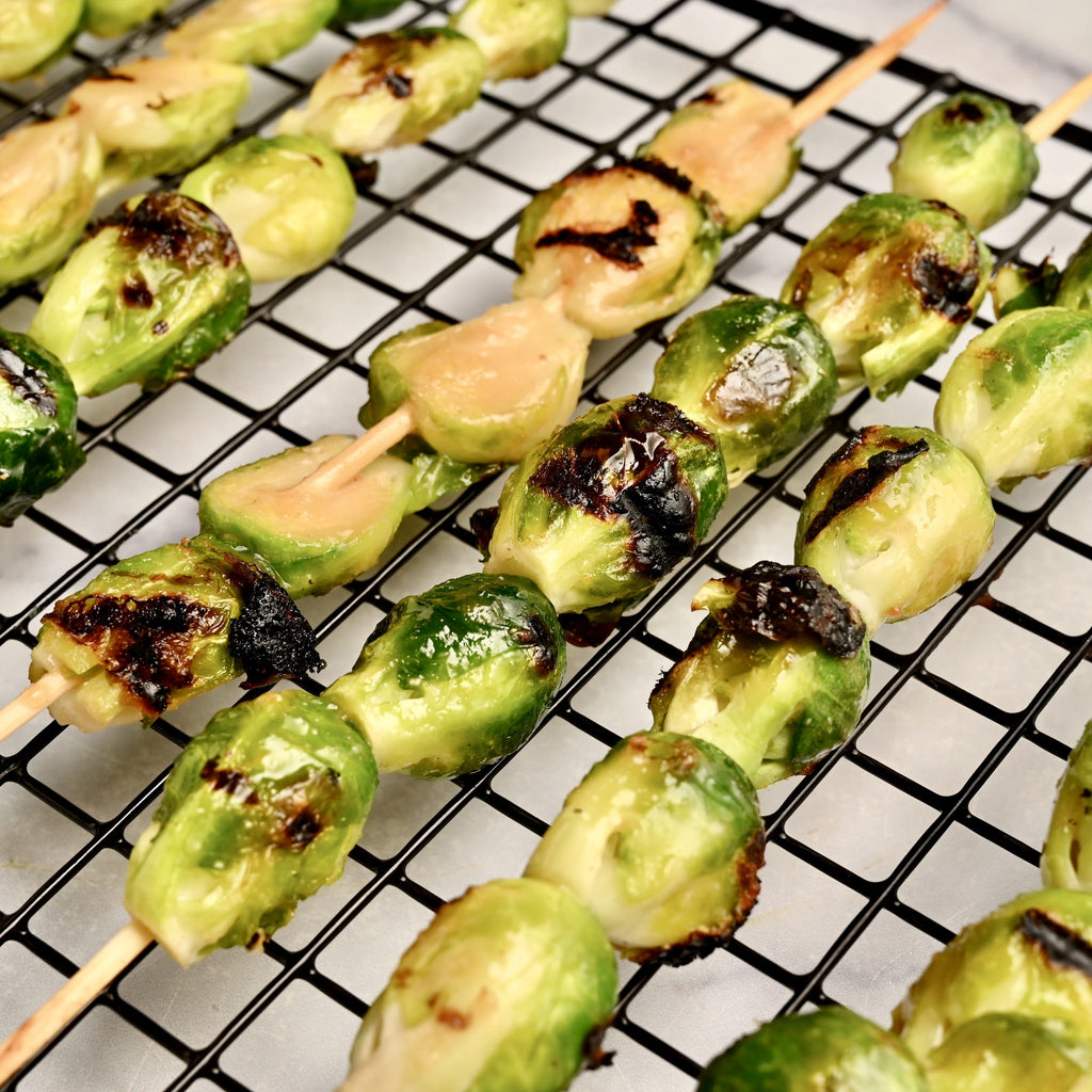 A close up of grilled Brussels sprouts on skewers and topped with a creamy peanut sauce