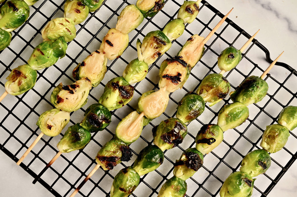 A close of grilled Brussels sprouts on skewers topped with a creamy homemade peanut sauce