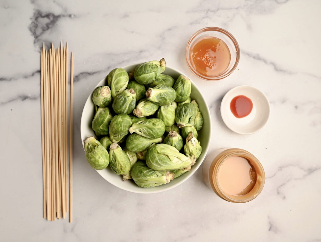 Wooden skewers next to a big bowl of raw Brussels sprouts