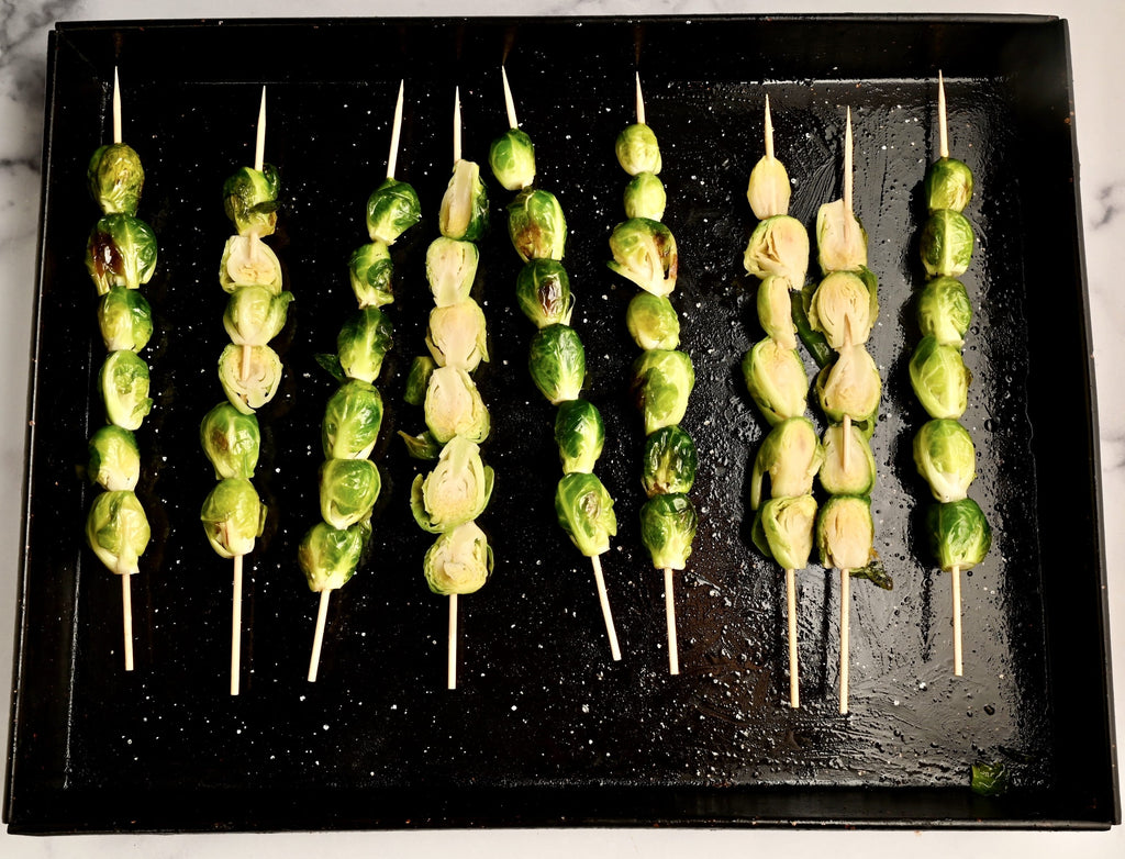 Raw Brussels sprouts on skewers placed on a black cooking sheet pan or tray