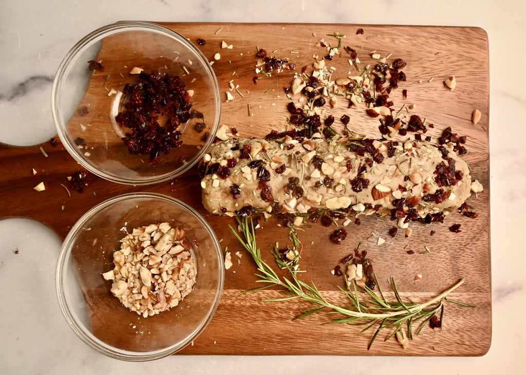 Dried cranberries and nuts being sprinkled onto a plant based cheese log