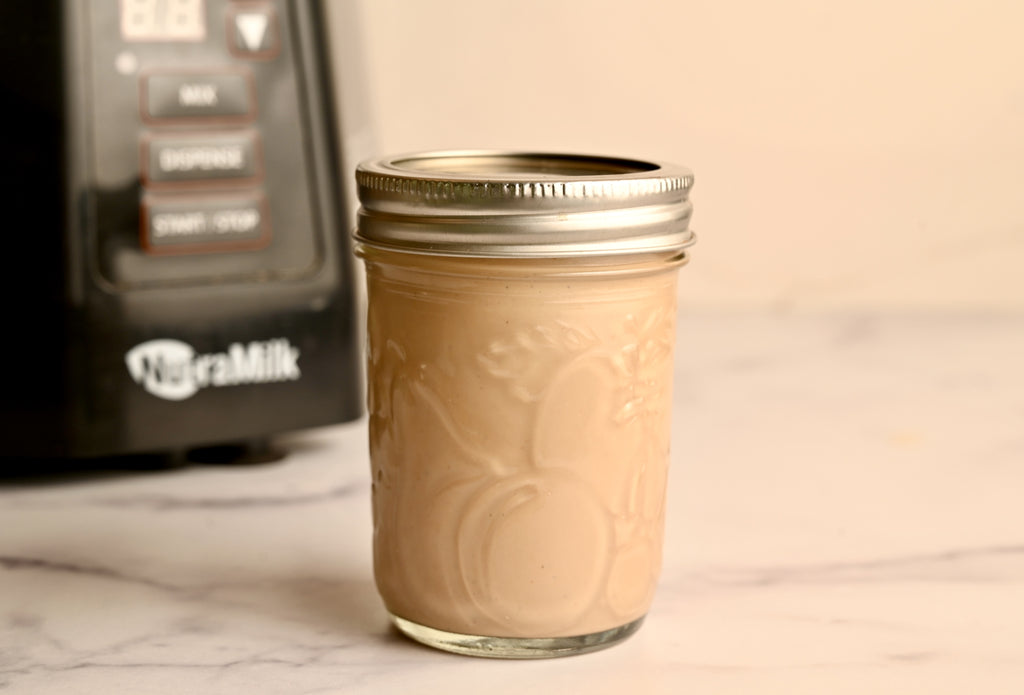 Homemade salad dressing in a glass jar with The NutraMilk in the background