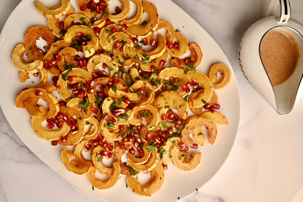 A white platter filled with delicata squash and bright red pomegranate seeds