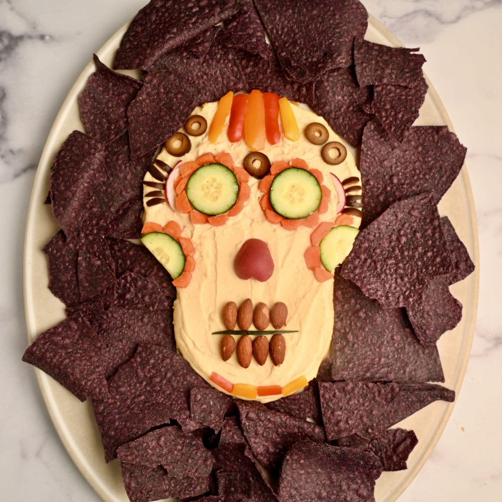 A skeleton hummus dip surrounded by blue tortilla chips