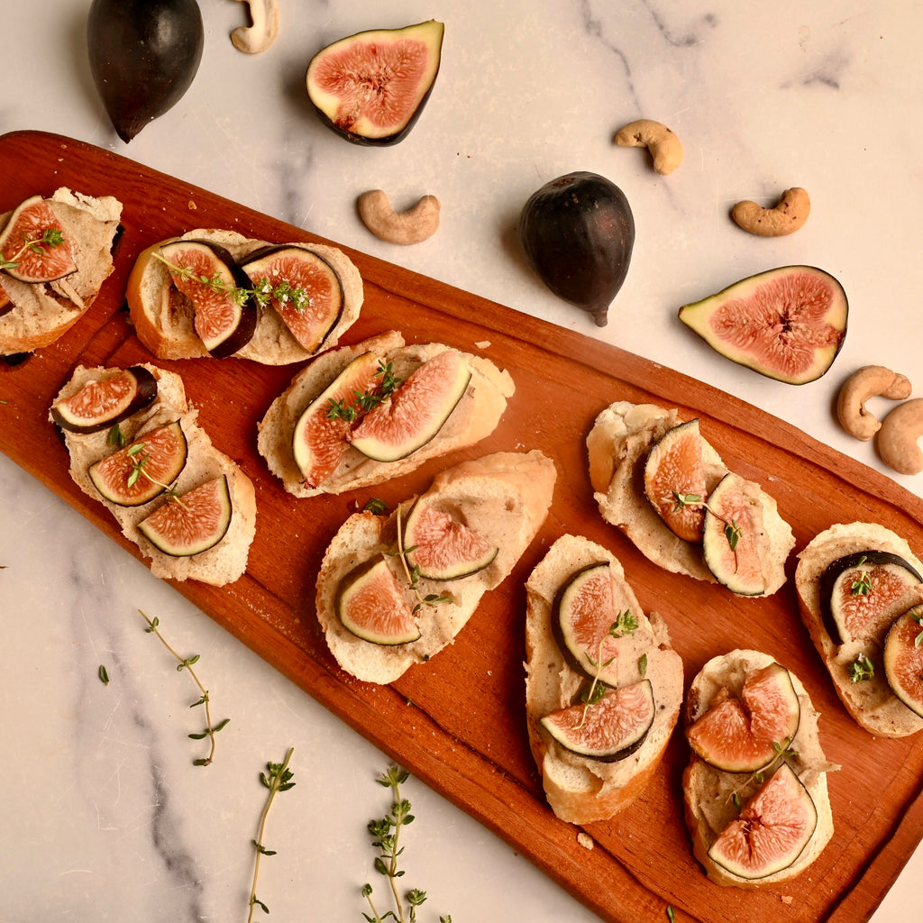 A close up of fig bruschetta on a wooden cutting board with sliced figs around it