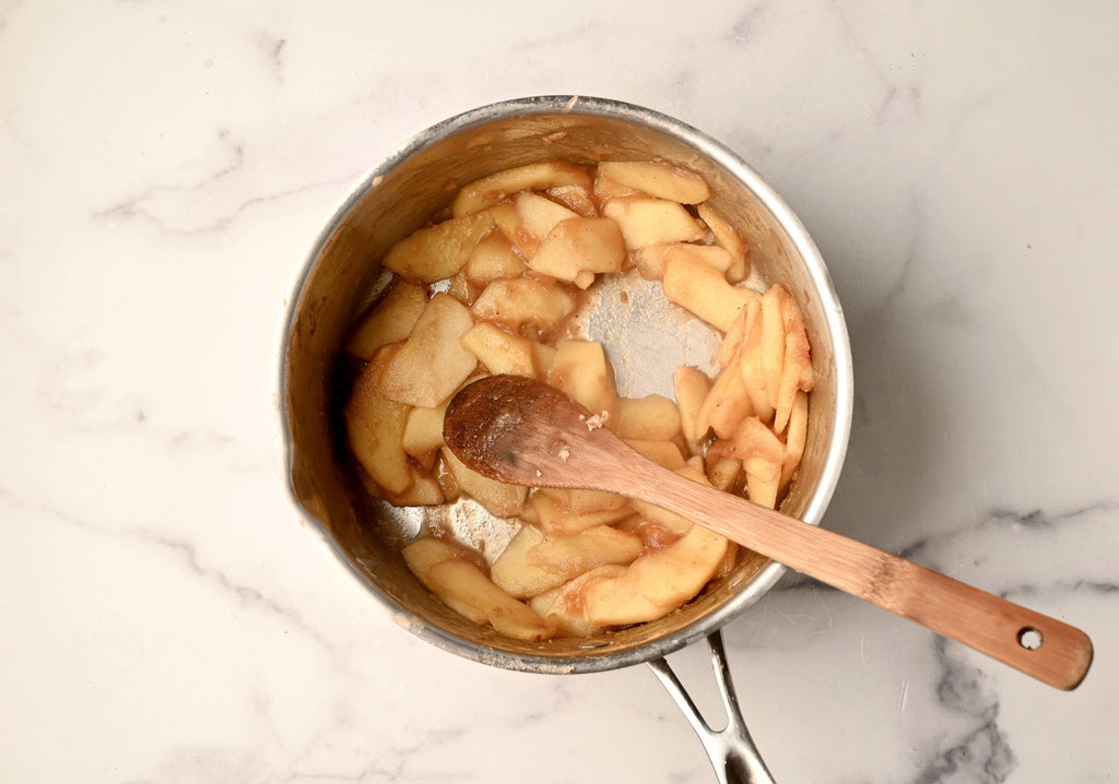 Raw apples being stirred in a big pot with a wooden spoon