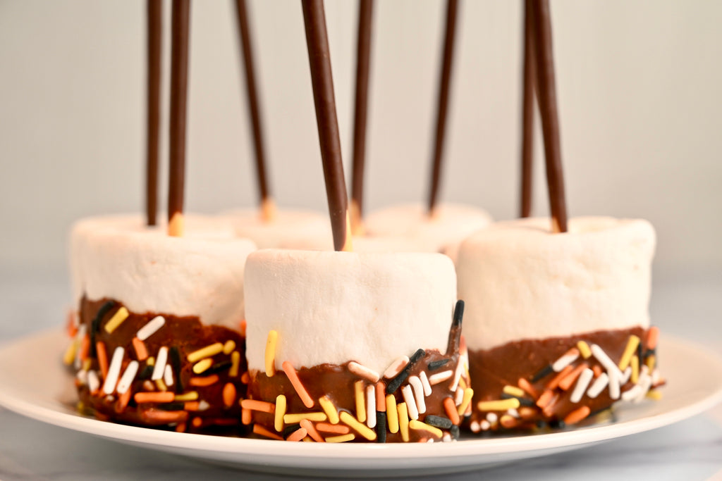 A plate of marshmallows dipped in chocolate with Halloween sprinkles