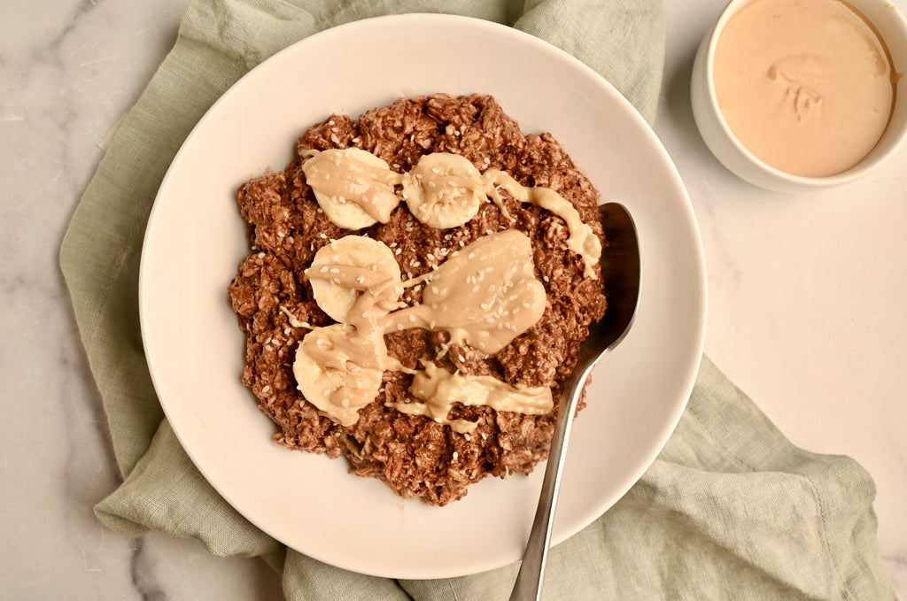 A bowl of chocolate overnight oats with bananas and nut butter with a green napkin under the bowl