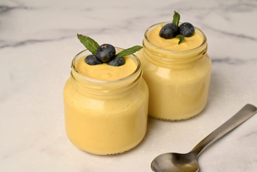 Clear glass jar filled with mango cashew pudding and topped with blueberries